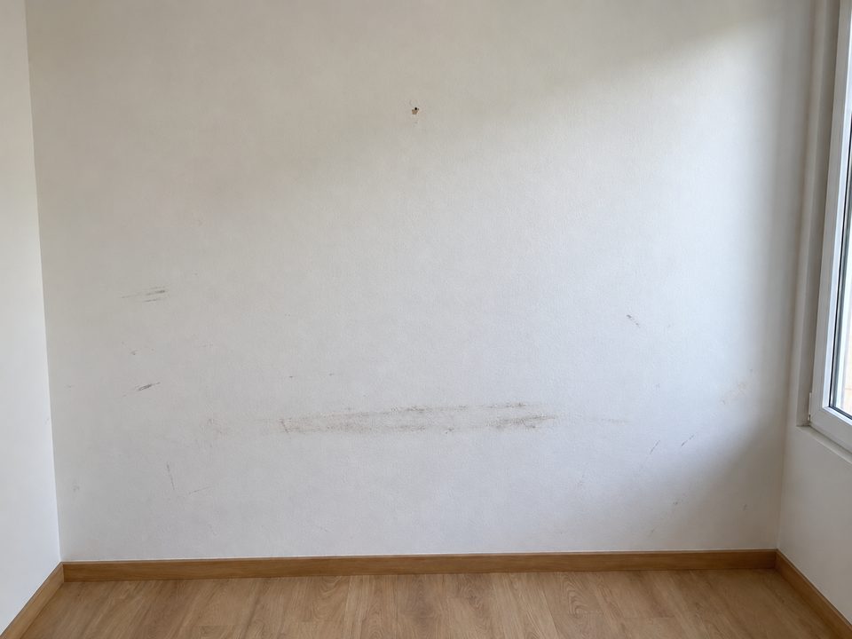 Same bedroom wall at move-out: scuff marks and a nail hole